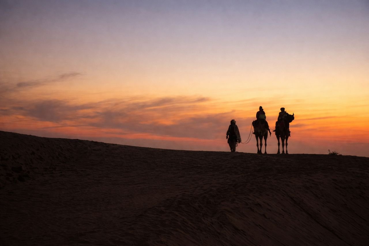 Silhouette of camels and riders during sunset in Sam, Rajasthan's Thar Desert.